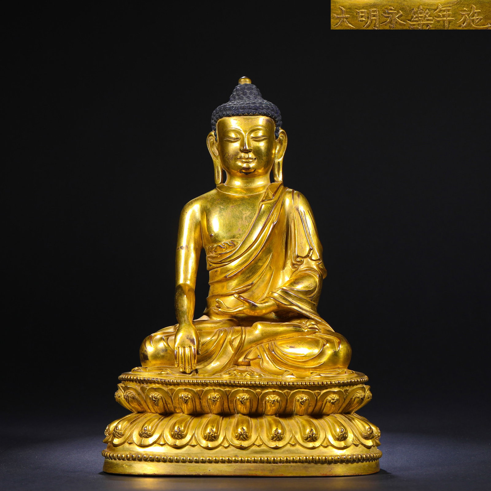 A GILDED BRONZE SITTING STATUE OF SAKYAMUNI BUDDHA WITH THE YONGLE INSCRIPTION OF THE MING DYNASTY: H:26cm(10.24in)W:17cm(6.69in)Weight:3350g This is a gilded bronze seated statue of Sakyamuni Buddha from the Yongle period of the Ming Dynasty, inscribed with "Made and offered in the Yongle year of t