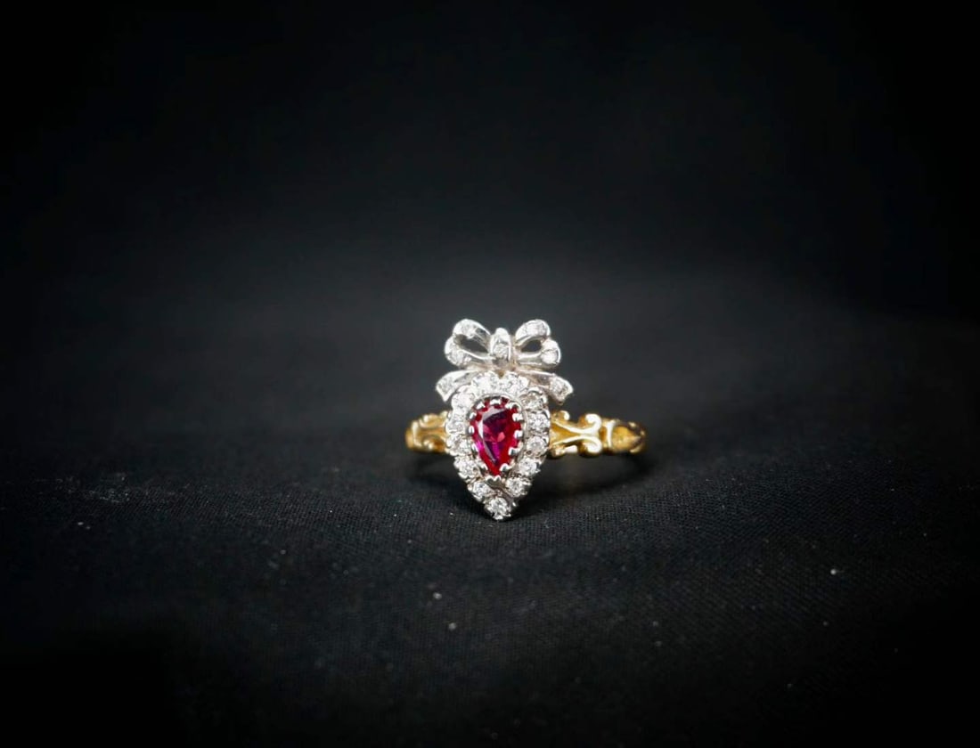 GEORGE VICTORIAN 18K GOLD RUBY HEART-SHAPED BOW ANTIQUE RING: This vintage ring from the British George Victorian period has been a romantic symbol for over a century. The ring is made of 18K gold, and the warm gold texture has been precipitated over the years, 