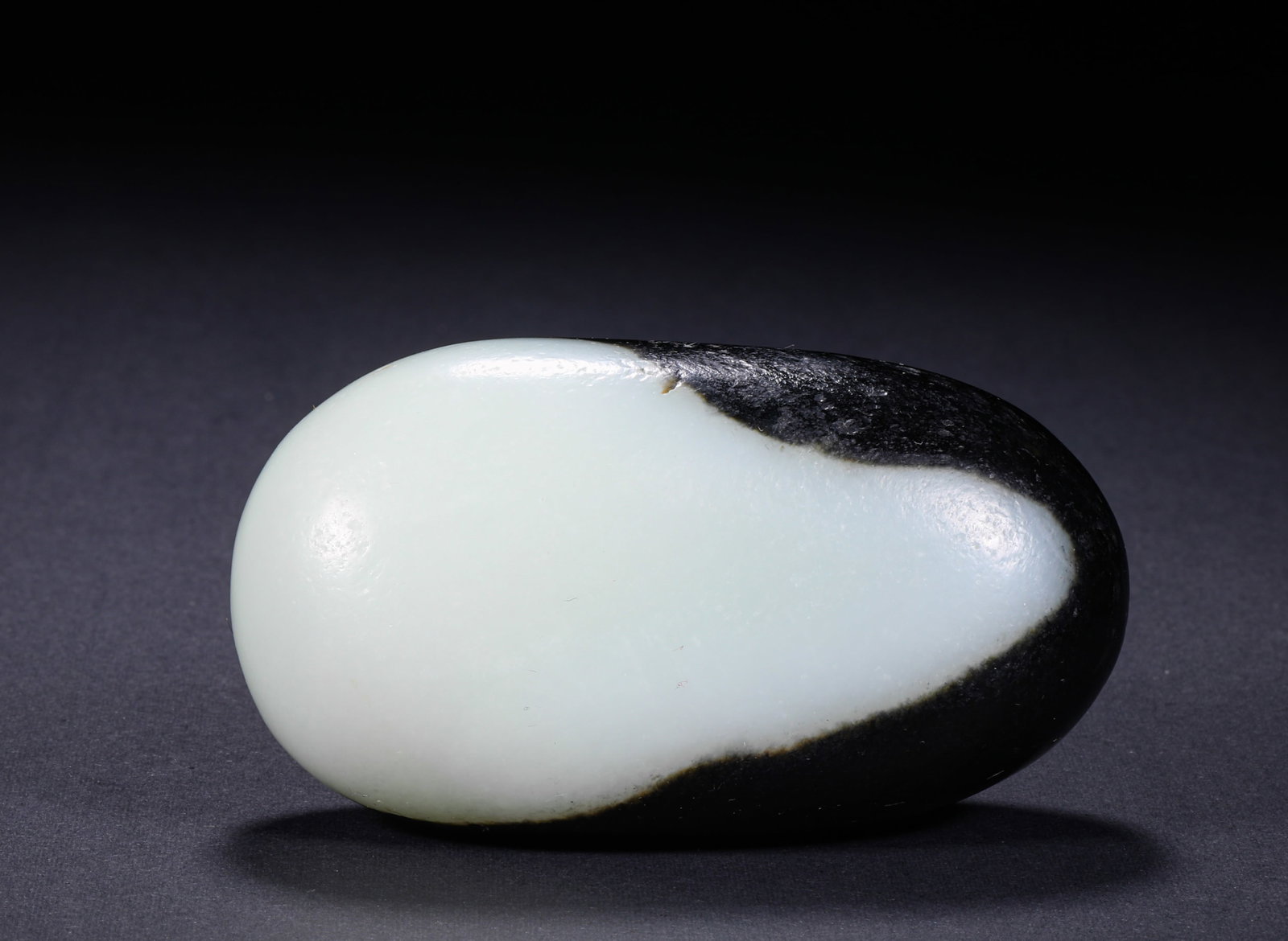 HETIAN JADE BLACK OIL SKIN SINGLE SEED ROUGH STONE: H:5cm(1.97in) W:8.5cm(3.35in) Weight:310g(0.68lb)Rare top-tier concentrated black oil skin, with rich deep moist black hue. It forms a natural distinct boundary "sky-earth skin" on the pebble edge, wi