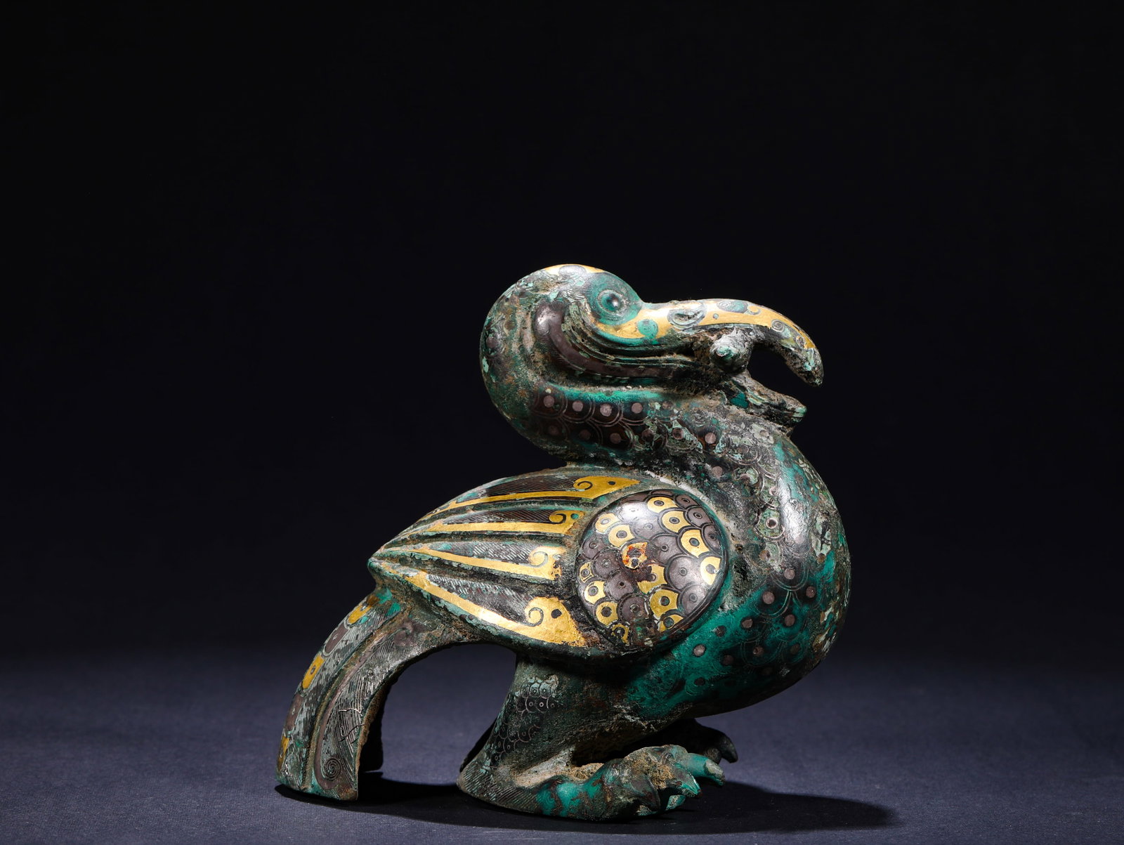 AN INLAID GOLD AND SILVER BIRD-SHAPED ORNAMENT FROM THE WARRING STATES PERIOD: H:10cmW:11cmWeight:780g This is a gold-silver inlaid mythical bird ornament, crafted from bronze with the classic gold-silver inlay technique prevalent from the Warring States Period to the Han Dynast