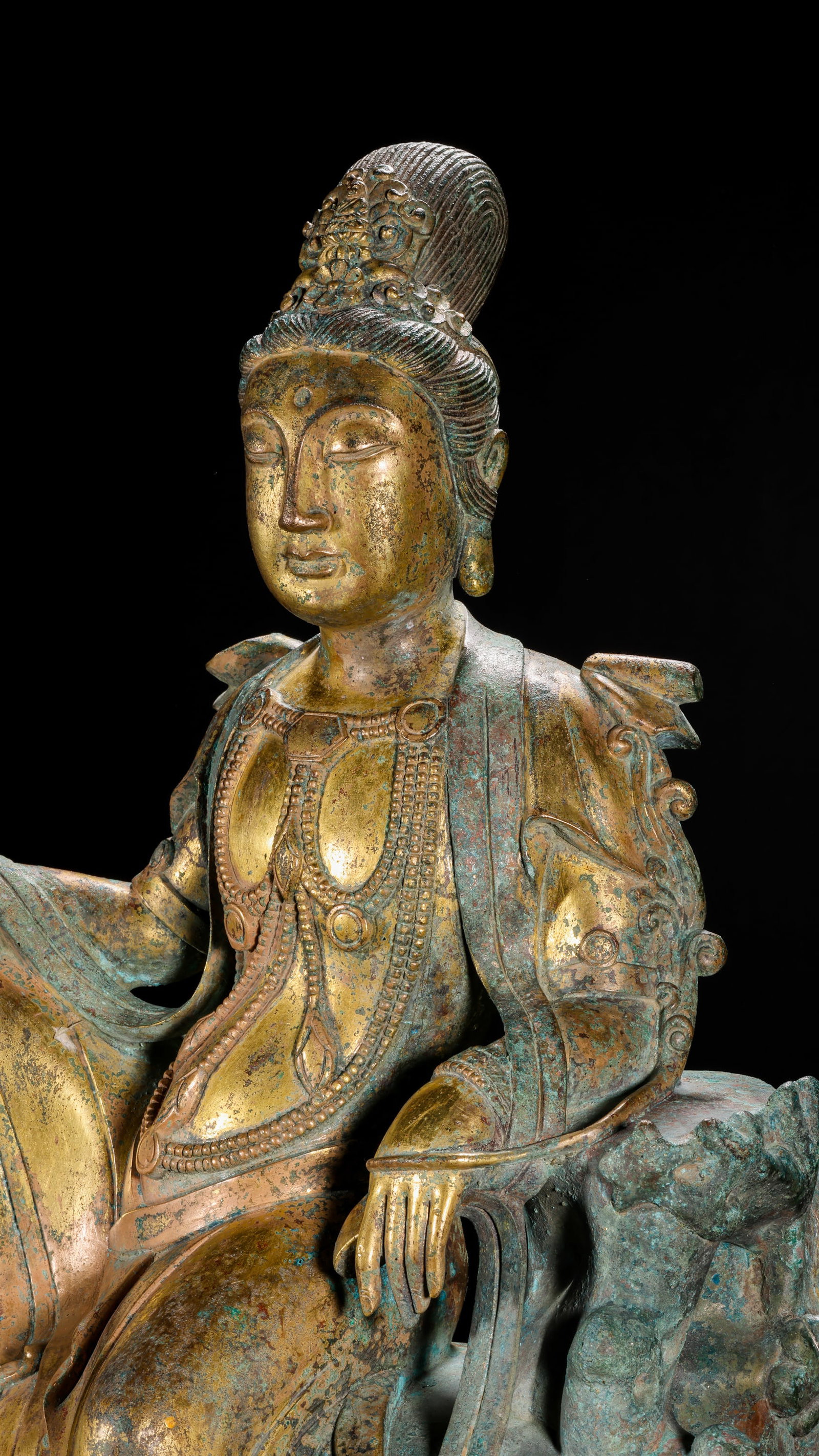 GILDED BRONZE SEATED STATUE OF GUANYIN IN THE MING DYNASTY: H:37cm(14.57in) W:25cm(9.84in) Weight:7170g(15.81lb)This statue is cast in bronze and gilded. Guanyin Bodhisattva sits comfortably on a rocky pedestal, wearing a precious crown with a compassionate fa