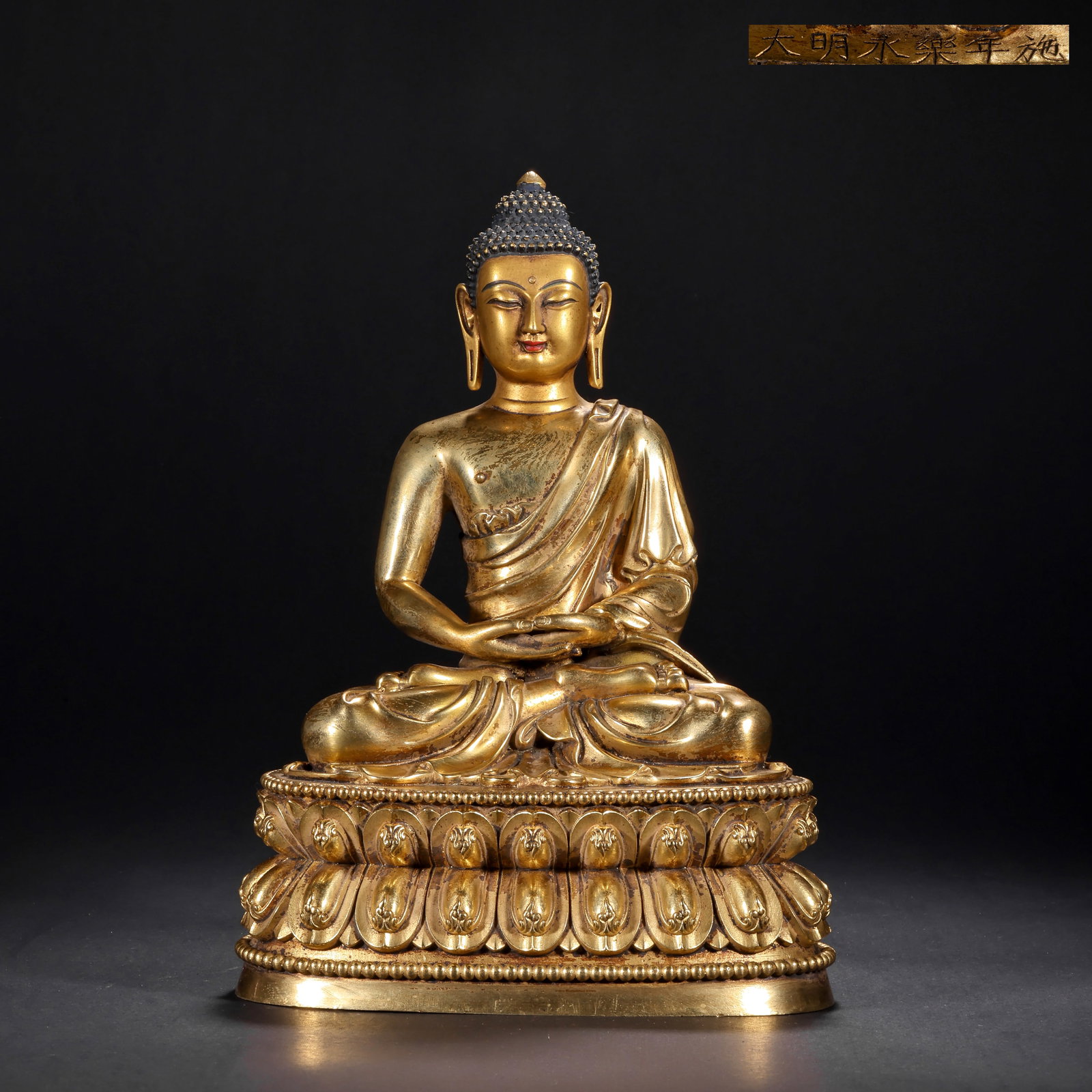 A GILDED BRONZE SEATED STATUE OF SAKYAMUNI BUDDHA FROM YONGLE, MING DYNASTY: H:22.0cm(8.66in) W:14.5cm(5.71in) Weight:1450g(3.20lb)This statue is cast in bronze and gilded. Sakyamuni Buddha sits in lotus position on a double lotus pedestal, with a high spiral hair bun and a co