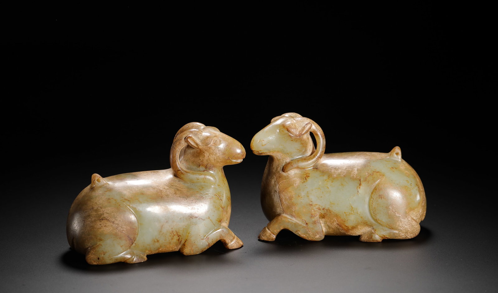 A PAIR OF SHEEP LYING DOWN IN HAN DYNASTY HETIAN JADE: H:7cm(2.76in)W:10cm(3.94in)Weight:910g(2.01lb)This is a pair of Han Dynasty jade recumbent rams, carved in the round in a kneeling pose with a docile and elegant form. They exemplify the realistic sty