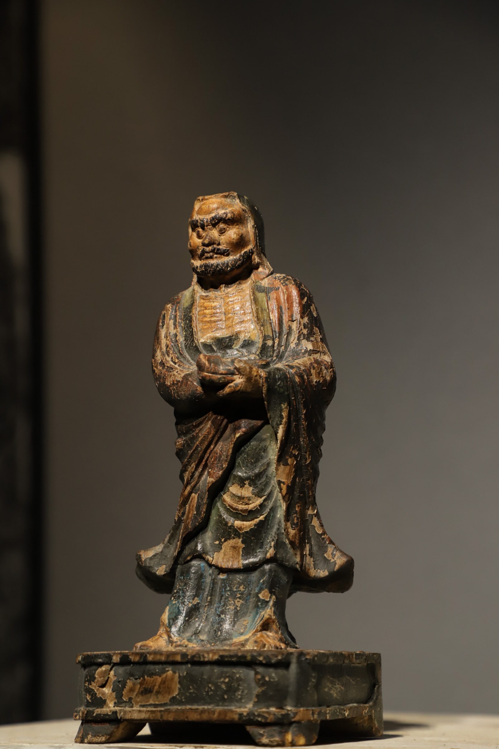 PAINTED WOOD CARVINGS OF BODHIDHARMA STANDING BUDDHA FROM THE MING DYNASTY: H: 27cm (10.63in) L: 12cm (4.72in) W: 11cm (4.33in): Solid wood carved Bodhidharma figure painted with black, brown and blue mineral pigments; aged lacquer peels partially off, equipped with original 