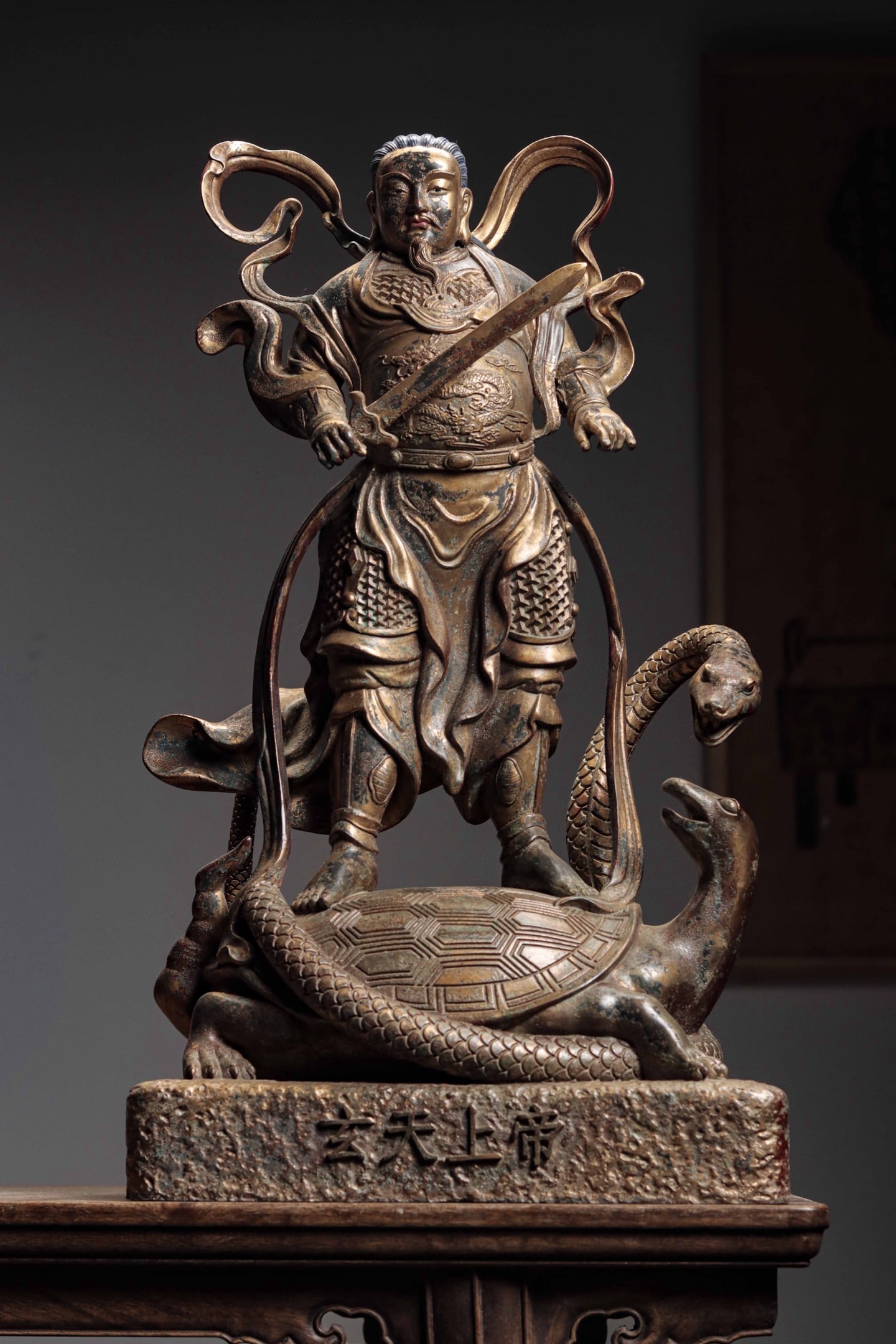 A GILDED BRONZE STATUE OF EMPEROR ZHENWU FROM THE QING DYNASTY: Weight: 12900g (28.44lb) H: 61cm (24.02in) W: 35cm (13.78in) T: 23cm (9.06in)Cast bronze with lacquer gilding; deity stands atop tortoise-snake Xuanwu, holding sacred sword, pedestal inscribed with de