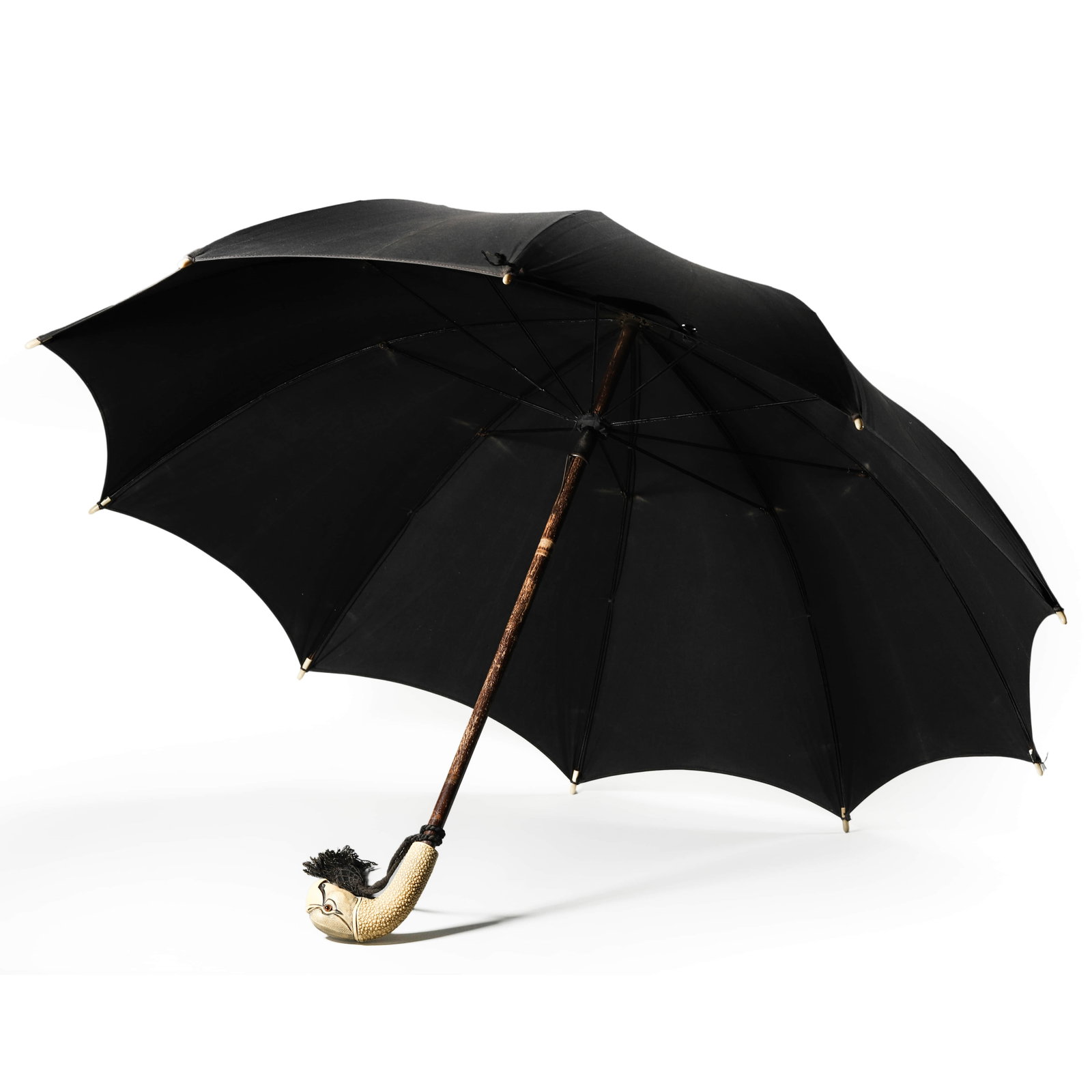 ANTIQUE BLACK PARASOL WITH CARVED HANDLE IN THE FORM OF A PARROT HEAD: Length: 24 1/4 in. (61.5 cm) An antique black parasol featuring a handle intricately carved in the form of a parrot's head, with detailed texturing and inset glass eyes. The material of the handle is