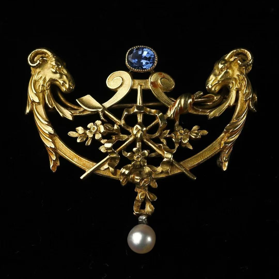Art Nouveau Period (1880-1920) French Chased 18K Gold Double Ram-Head Sapphire and Natural Pearl: 3.7*4.1cm Wt:14.64g Hand-crafted entirely in 18K gold, featuring hand-chased three-dimensional twin ram-heads within a floral-drapery composition. A Sri Lankan unheated sapphire is set at the top, and