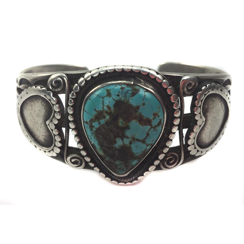 Navajo Turquoise and Ingot Silver Bracelet: Navajo Turquoise and Ingot Silver Bracelet with Heart Designs c. 1920s, 55 grams, 1" bandwidth, size 7 to include a gap of 1". The turquoise stone measures 22mm x 18mm (0.86" x 0.7"). This bracelet is