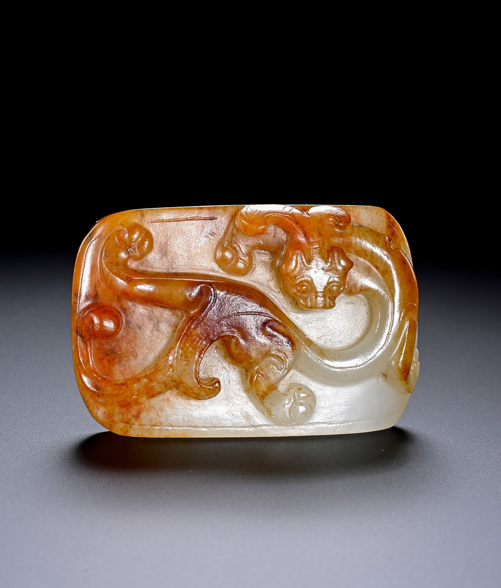 A WHITE JADE 'RED-STAINED CARVED CHI-DRAGON' SWORD FITTING: A WHITE JADE 'RED-STAINED CARVED CHI-DRAGON' SWORD FITTING Description: Dimensions: Width: 4.6 cm x Height: 3 cm. All measurements are approximate.
