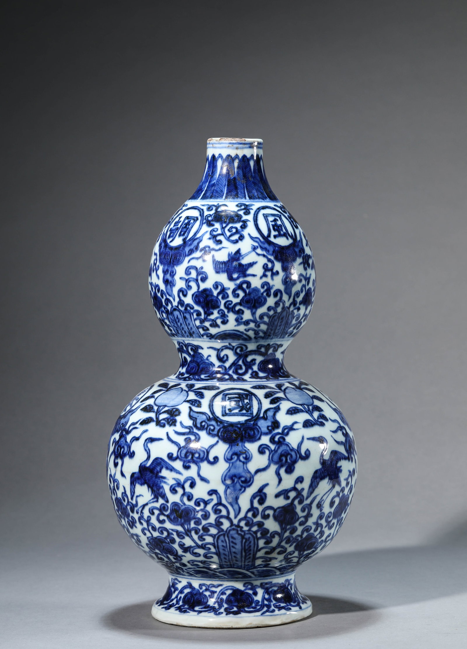 A BLUE AND WHITE 'CRANES AND CLOUDS WITH 'GUO TAI MIN AN'' DOUBLE-GOURD VASE: A BLUE AND WHITE 'CRANES AND CLOUDS WITH 'GUO TAI MIN AN'' DOUBLE-GOURD VASE Description: Dimensions: Width: 19.1 cm x Height: 37.5 cm. All measurements are approximate.