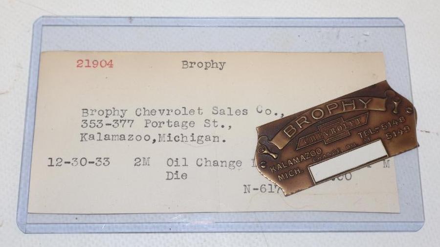 N.O.S. BROPHY CHEVROLET STAMPED OIL CHANGE REMINDER WITH BOW TIE GRAPHIC.: 2.5" X 1". 1933 NEW OLD STOCK SAMPLE OIL CHANGE REMINDER FOR BROPHY CHEVROLET IN KALAMAZOO, MICHIGAN. ALSO INCLUDED WITH THE REMINDER IS THE ORIGINAL DESCRIPTION CARD. CONDITION: BRILLIANT NEW OLD STO
