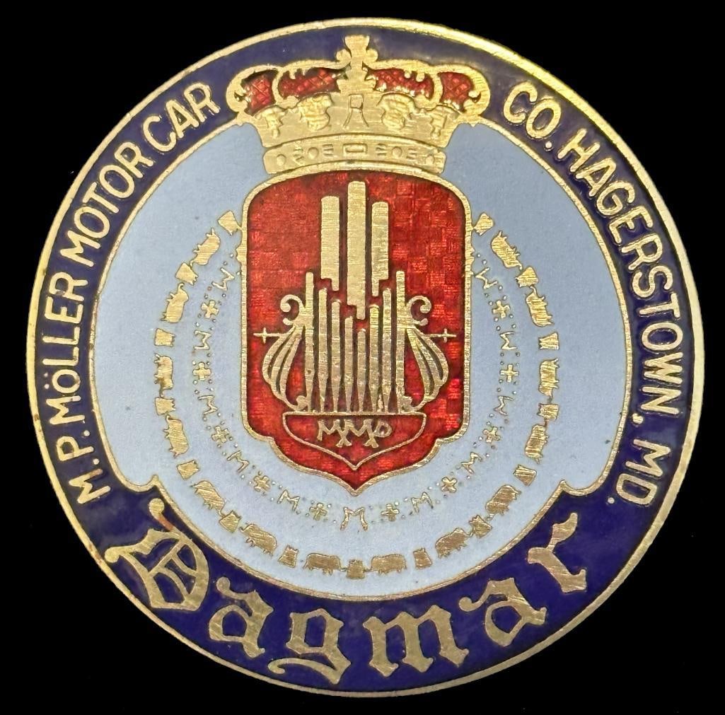 Dagmar Radiator Emblem: 1924 - 1926 Dagmar radiator emblem. This emblem looks to be New Old Stock (NOS) and has the proper metal pattern beneath the transparent red enamel. It is rated scarce and measures approximately 2.5"