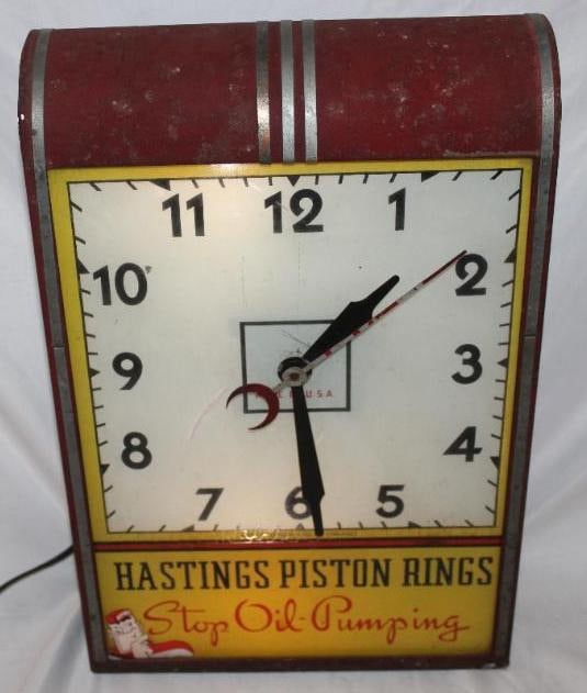 Hastings Piston Rings Light Up Advertising Clock: This clock was produced by the Crystal Manufacturing Co. It has a reverse painted glass face front with some minor wear and crazing throughout. The image on the lower left corner is a decal attached t