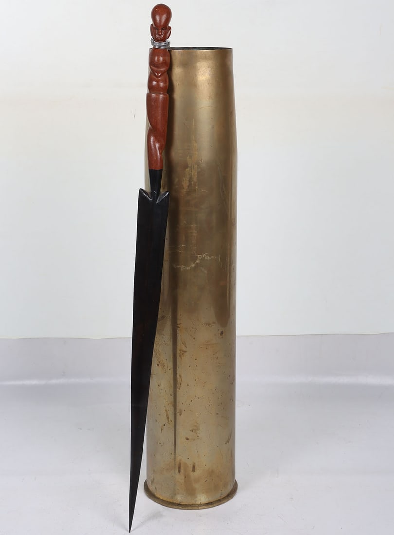 Large Shell Case: Large Shell Case: Heavy large brass shell case with stamping to base being 18.5 cms wide complete with primer and 85 cms tall and a carved wood African style spear point. 2 items NOT AVAILABLE TO BIDD