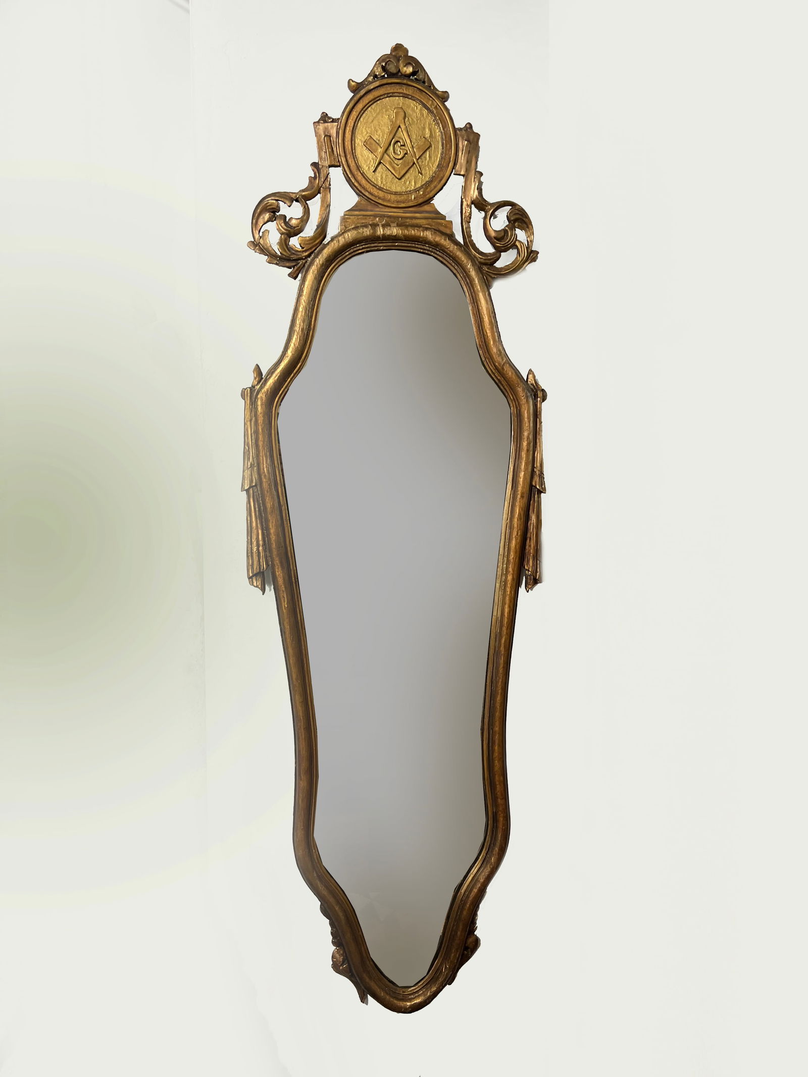 Vintage Masonic Giltwood Pier Mirror | 45" Tall Fraternal Wall Mirror with Square & Compasses Emblem: This striking 45-inch tall vintage mirror features a distinctive silhouette and ornate gold-leaf finish, centered by a prominent Masonic crest. Its elongated "pier mirror" form was traditionally desig