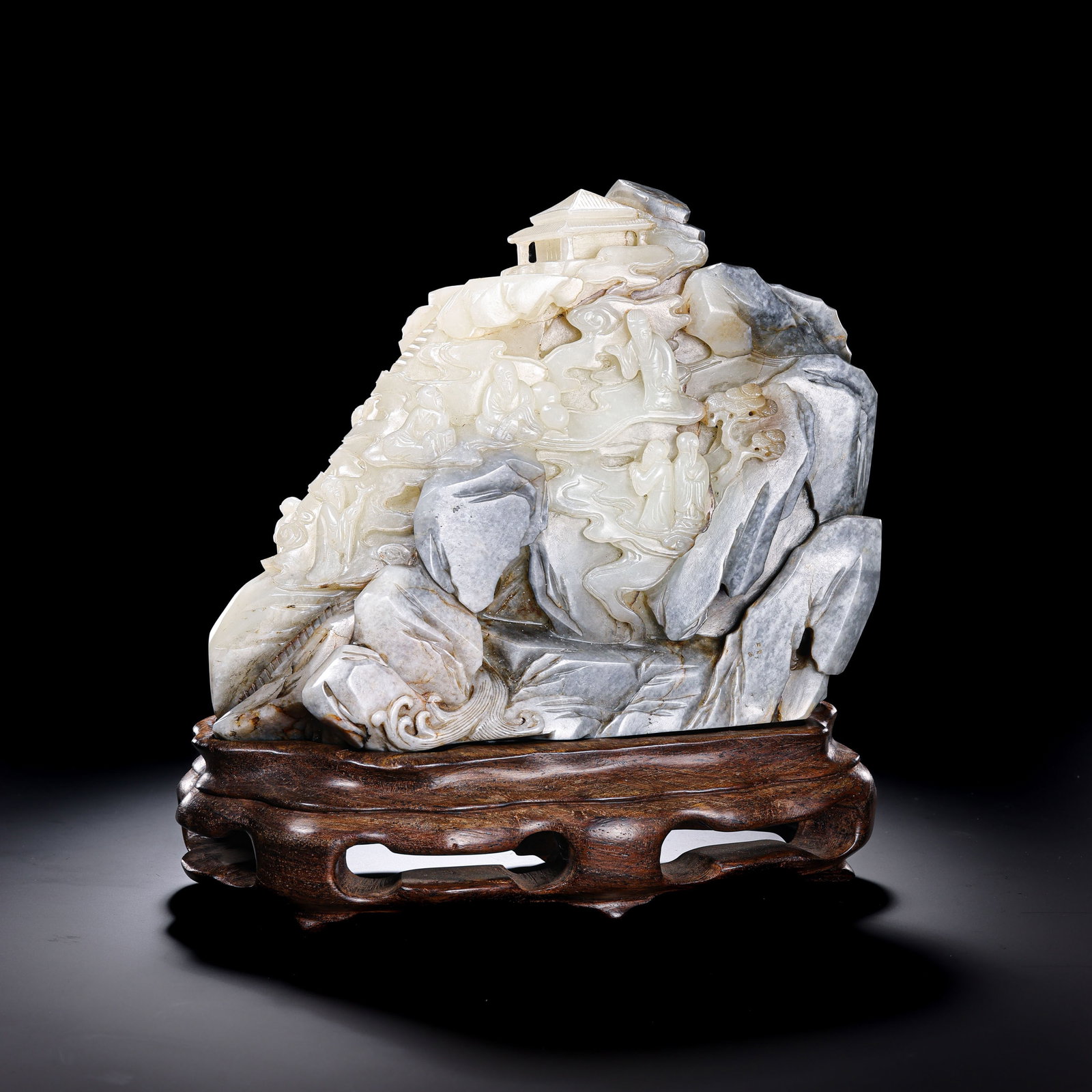 A Chinese Qing Dynasty Hetian Jade Mountain Boulder Carving with Scholars in a Landscape: Height: 18.5 cm; Width: 21.5 cm; Weight: 2852 gCondition and Provenance?In good overall condition. The piece is carved from a substantial section of Hetian jade and is presented on a fitted wooden sta