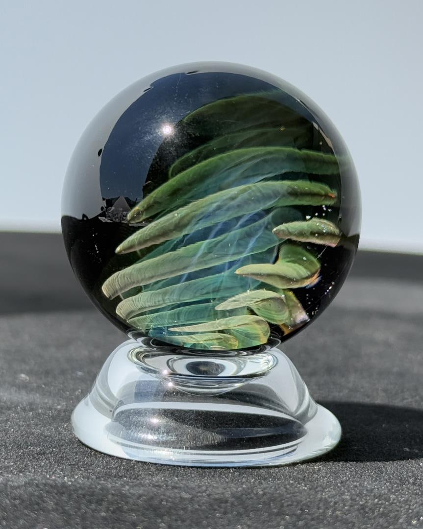 Tanner Castle Glass Borosilicate Marble: Title is Lama Sweeping Implosion #3. 1 7/8" diameter. Tanner Castle is an American glass artist renowned for his intricate and mesmerizing borosilicate marbles that blend technical mastery with a deep