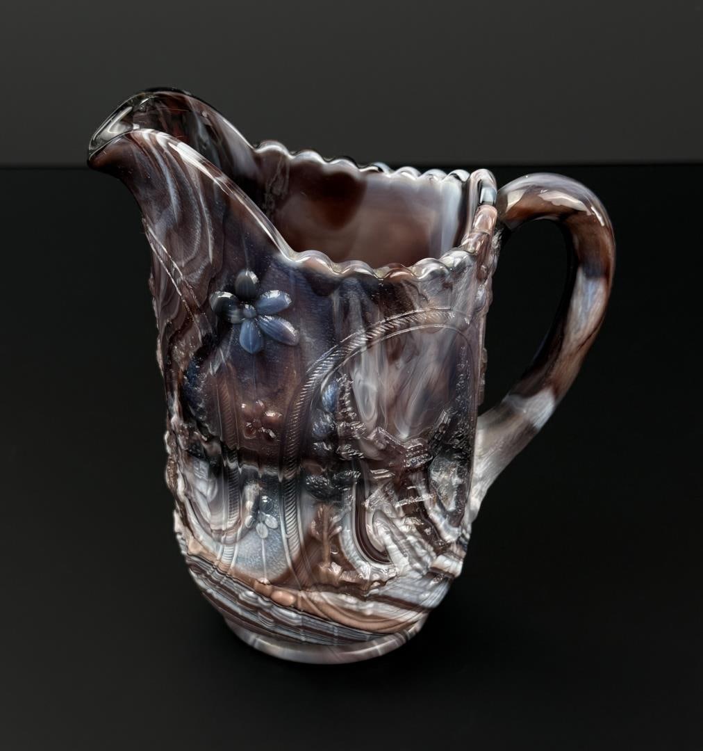 Imperial Glass Co Purple Slag Glass Pitcher: 6 1/2" by 4 1/2" by 4 1/2". Shows a windmill pattern featuring embossed scenes of houses, boats, and flowers.