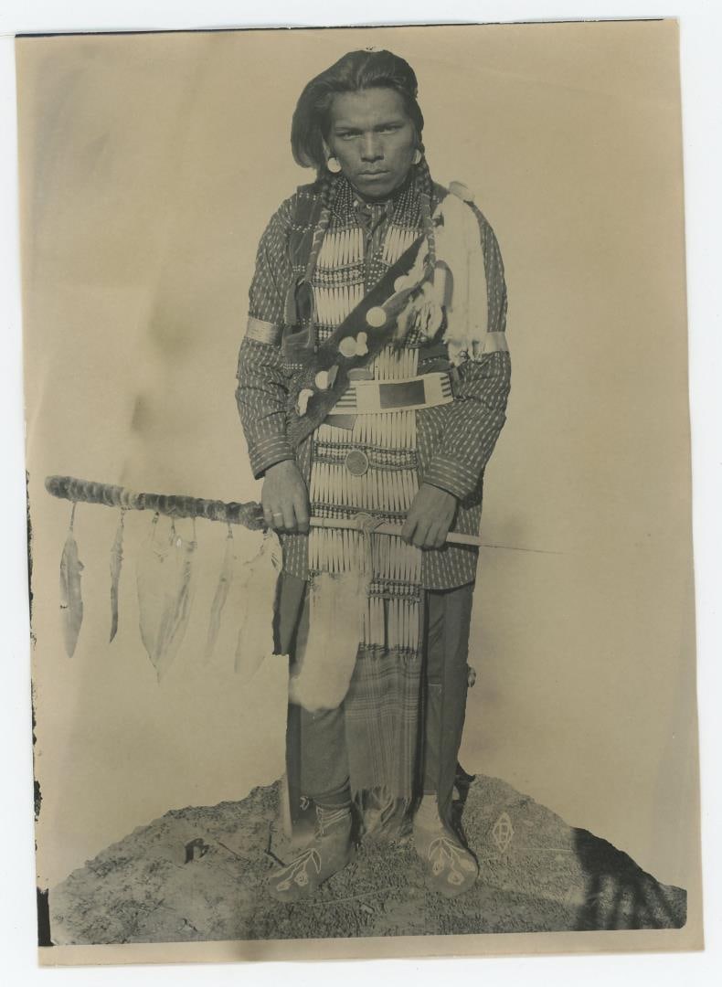 Edward Boos Flathead Indian Montana Photo: 5" by 7". Indian man, Snots-ee (earings), dressed in an elaborate costume and holding a short spear with a number of hanging feathers. Boos' Flathead Reservation portraits document particularly insigh