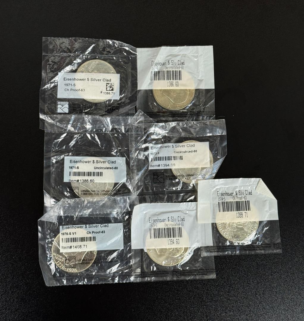 Lot of 7 Silver Clad Eisenhower Dollars: Lot of seven Eisenhower silver-clad dollar coins, all housed in protective plastic packaging from Littleton Coin Co.