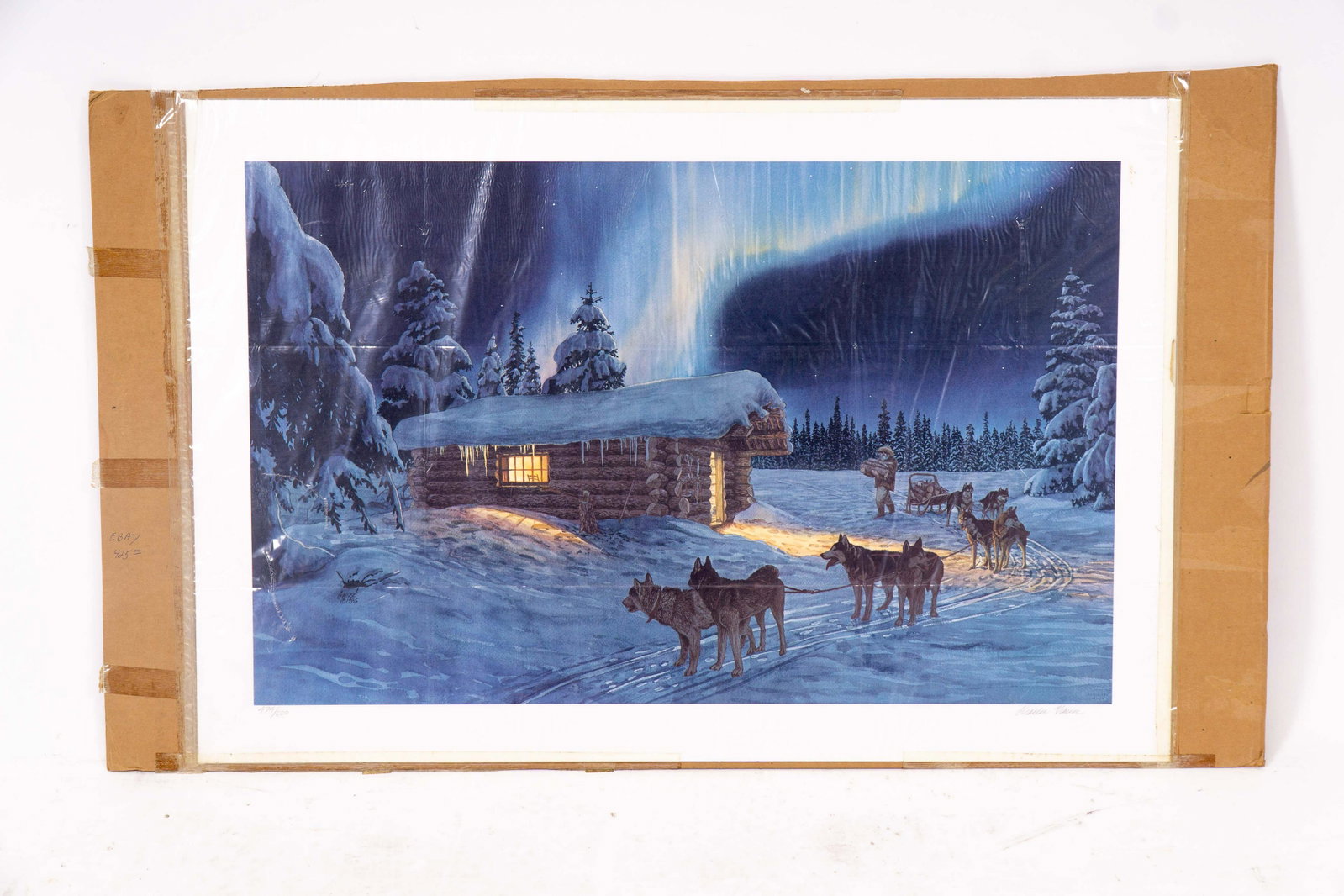 Signed Limited Edition Dog Sled Print: Print of watercolor painting depicting a team of sled dogs beside a log cabin, with a man carrying wood logs, signed in pencil in the lower right and numbered 474/500 in the lower left. Unframed, in p