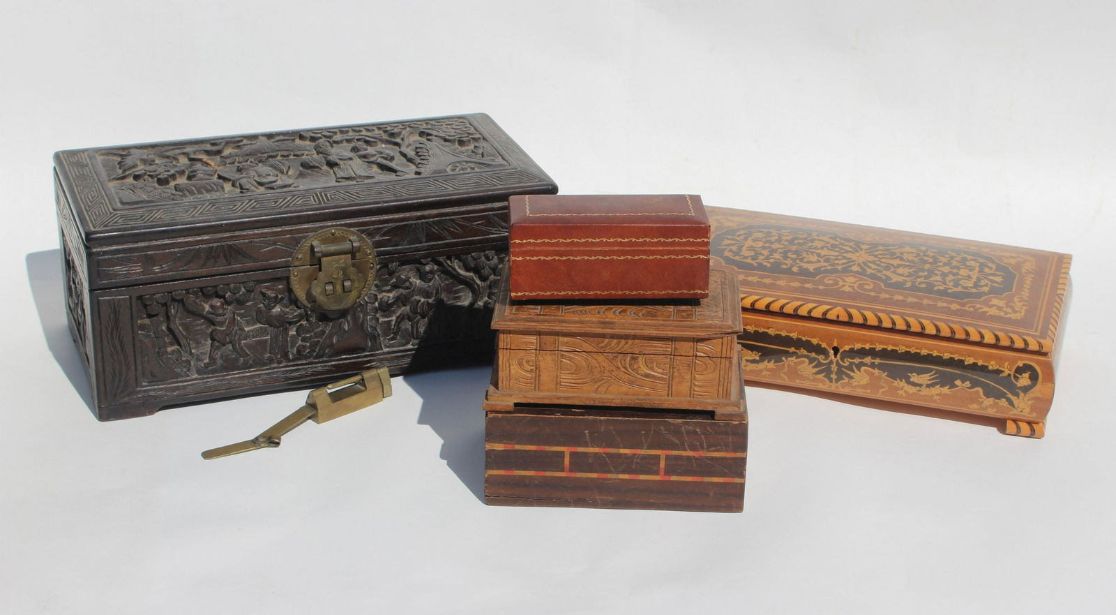 LOT OF 5 ASSORTED WOODEN BOXES: Inlaid wooden music box from Capri in good condition, 10 x 6, carved Chinese box w/brass lock. One area on top scene has damage, 5.75 x 11, 3 other small boxes one being a puzzle box the small carved