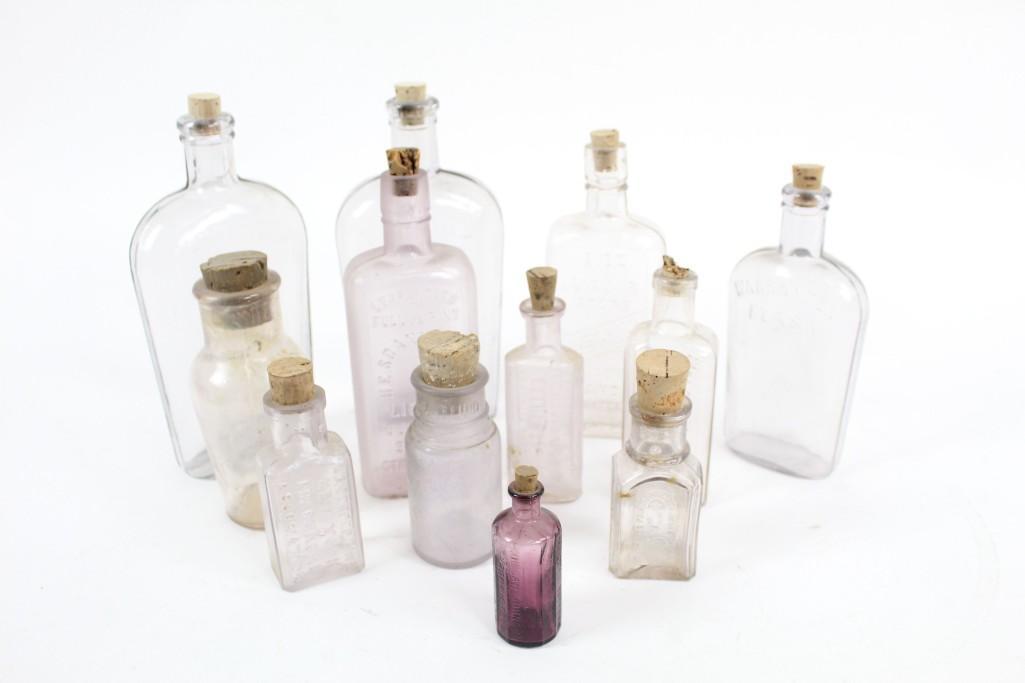 Lot 12 Misc. Antique Lavender Glass Bottles with Corks: Lot of 12 misc antique lavender glass bottles with corks. These bottles all have their corks. There are flasks, biters, and pharmaceutical bottles with labels like "Sloan's Liniment Kills Pain" and "E