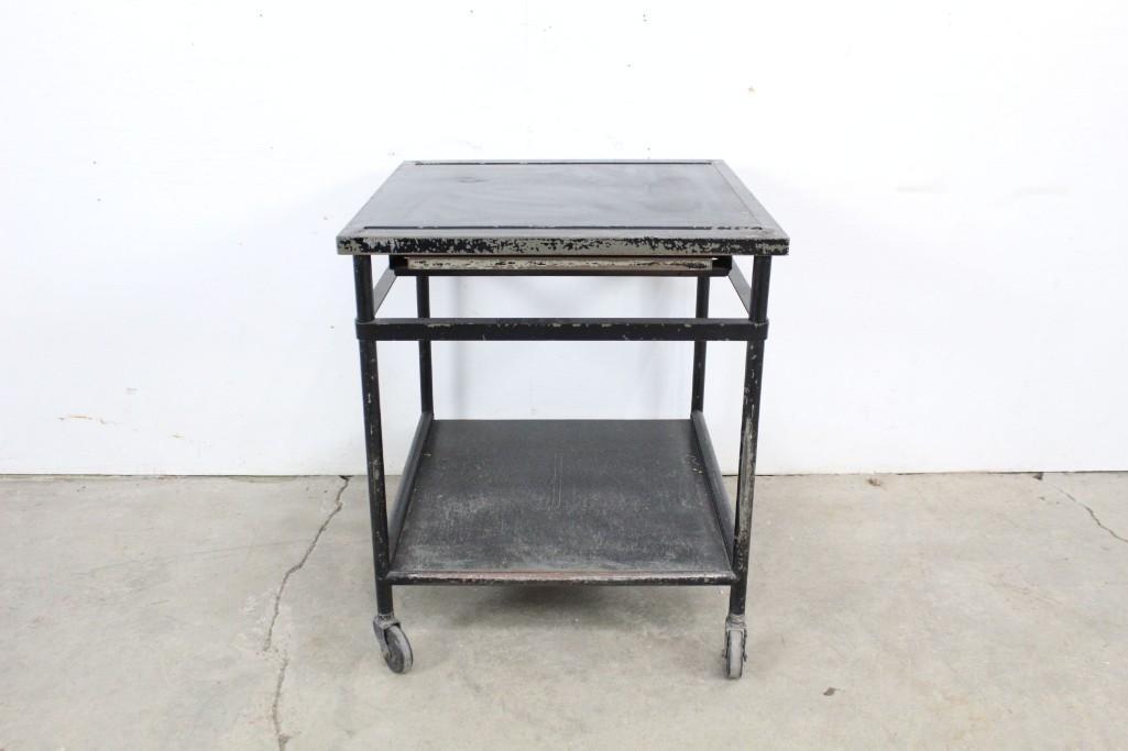 Industrial Metal Black Cart Stand Work Table on Wheels: Industrial metal cart or table stand on caster wheels, painted black, with two tiers, the top one featuring indentations for holding writing implements or small hand tools, as well as a pull-out surfa
