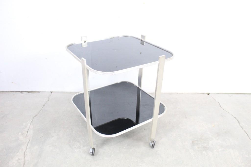 Art Deco Metal & Black Glass Rolling Bar Cart: Art Deco silver-plated rolling glass stand with two tiers. The stylish chrome-plated wheels, black-shaded translucent glass, and legs that are subtly offset from center combine to give this small stan