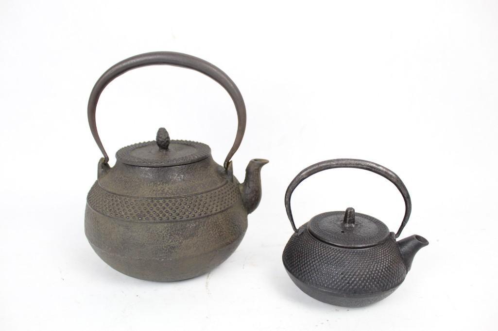 Pair of Cast Iron Japanese Teapots w/ Handles: Pair of Cast Iron Teapots with raised dot pattern on both, featuring lettering under spouts. Large teapot features a pineapple shaped handle. The dimensions for the large teapot are 8in h, 6.5in w, an