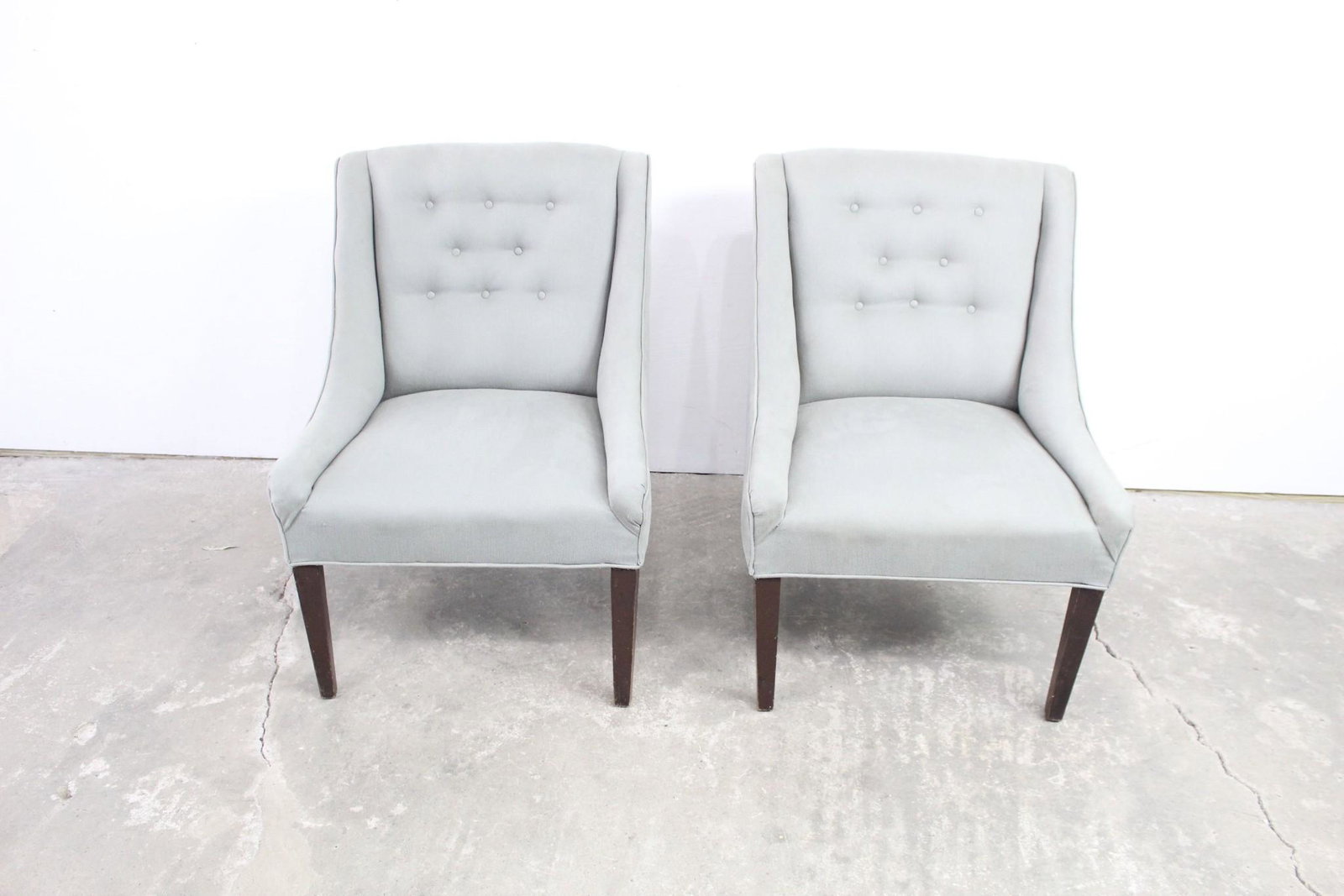 Pair of Gray Upholstered Sloped Arm Dining Chairs: Pair of Gray Upholstered Sloped Arm Dining Chairs. Attractive chairs have buttons on the backs and dark wooden legs for comfort. Use at your dining table for comfortable seating, or as extra seating i
