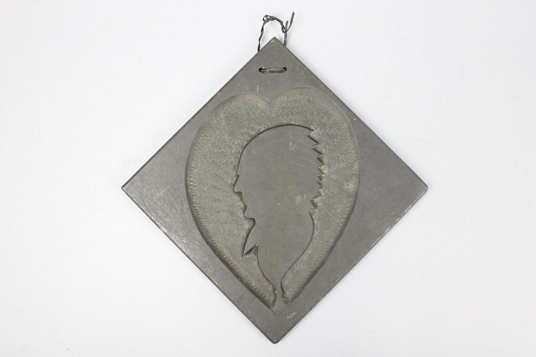 Folk Art Carved Stone Wall Sculpture of Native American Man: Folk Art Carved Stone Wall Sculpture of Native American Man. This is a black stone wall sculpture of a Native American man wearing a headdress. The profile portrait is inside of a heart shape. It hang