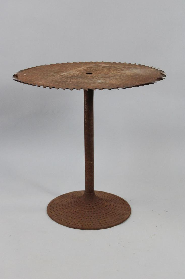 Industrial Saw Blade Found Art Cafe Patio Table: Industrial Saw Blade Found Art Cafe Patio Table. Table top made of a single large coarse tooth lumber mill saw blade, welded to a metal shaft on a round raised hobnail base, all with a heavy patina of