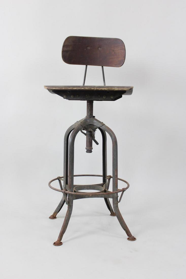 Industrial Toledo Drafting Stool: Industrial Toledo Drafting Stool. This stool with wood seat and back rests, metal tightening knob on the back. Adjusts up and down.Dimensions are 40 in h x 16 in w x 16 in d. Condition is good, stains