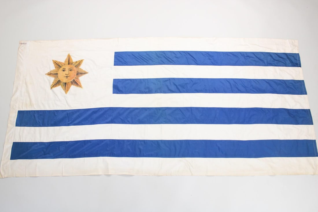 Large Uruguay Flag, Hand Painted Sun of May: Large Uruguay Flag, Hand Painted Sun of May. The national flag of Uruguay, made of satin with nine alternating blue and white stripes and a hand painted Sun of May. "Uruguay" is stenciled on one corne