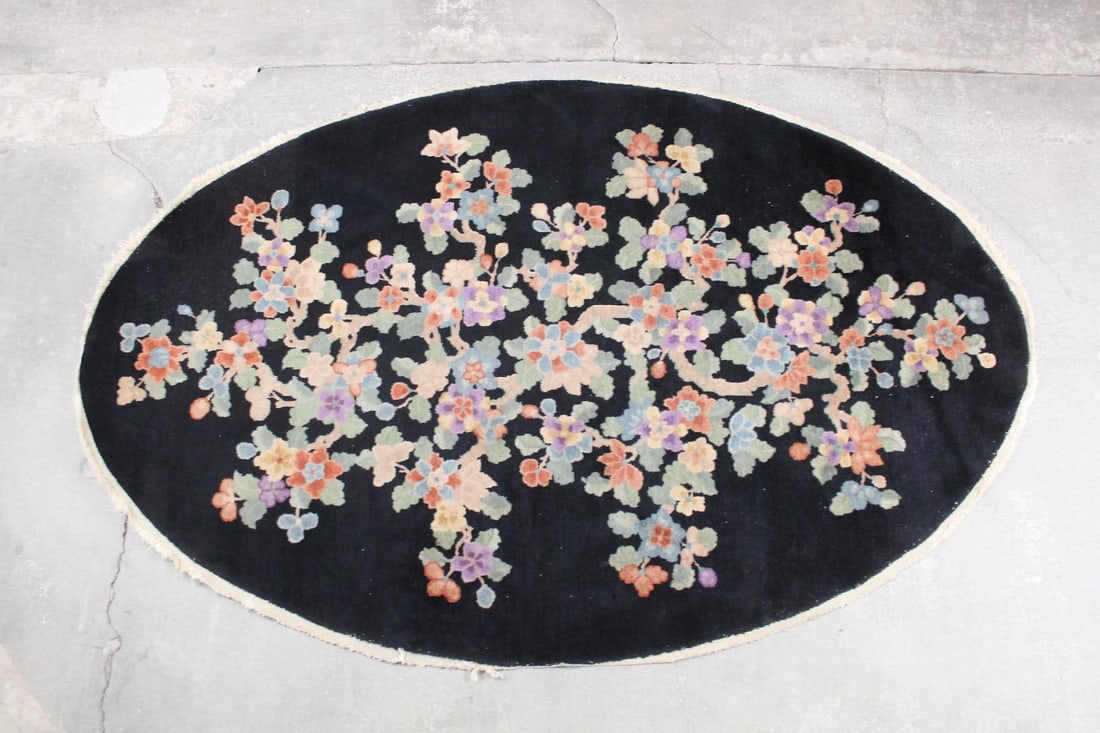 Oval Deco Asian Style Floral Rug: Oval Asian Style Floral Rug. This rug has short fringe along the edges and a black background, with colorful Chinese style flower blossoms all over in pastel shades. Dimensions are 59.5 in h x 95 in w