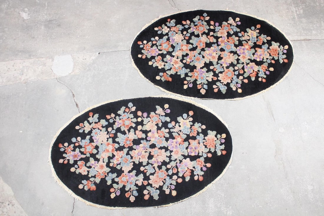 Pair of Oval Deco Asian Style Floral Rugs: Pair of Oval Asian Style Floral Rugs. These 2 rugs have short fringe along the edges and black background, with colorful Chinese style flower blossoms all over in pastel shades. Dimensions are 36 in h