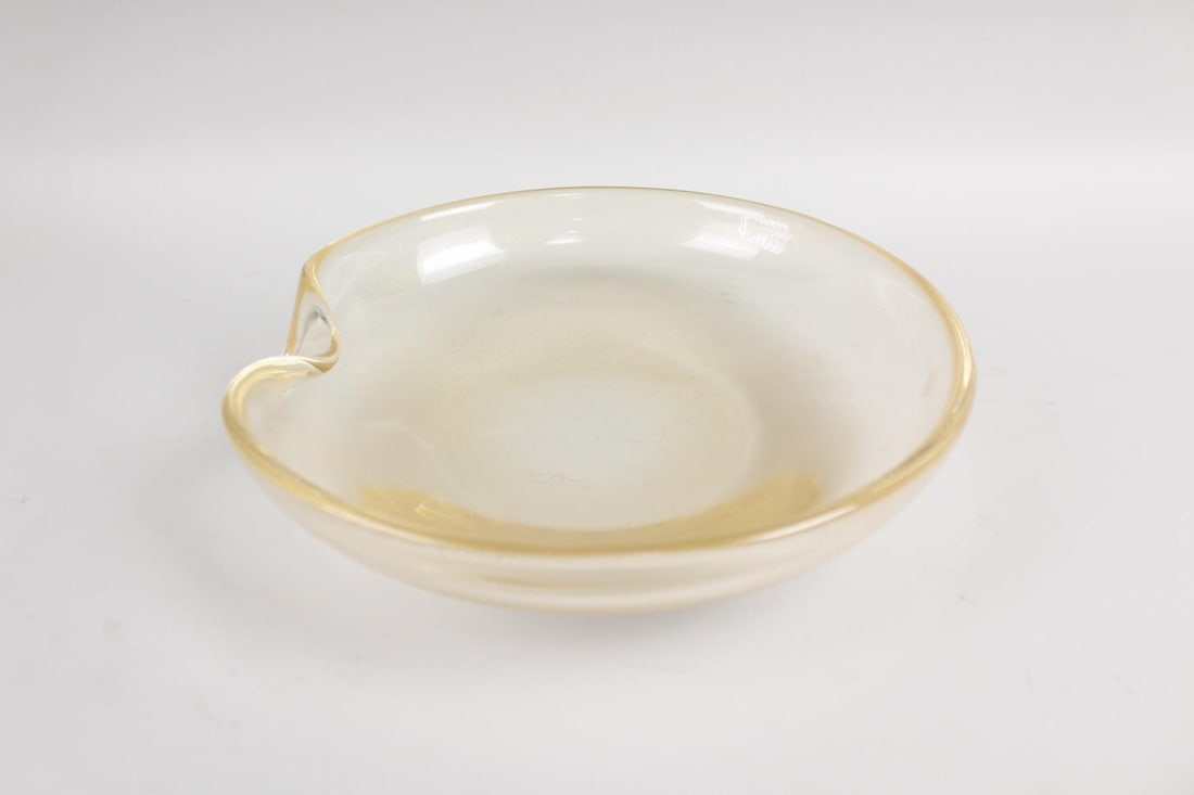 Signed Gold Speckled Glass Ashtray Dish, Elsa Peretti for Tiffany: Signed Gold Speckled Glass Ashtray Dish, Elsa Peretti for Tiffany. This round shallow dish of clear glass has golden specks throughout and a gilded rim, with a small dent for resting a cigarette. Mark