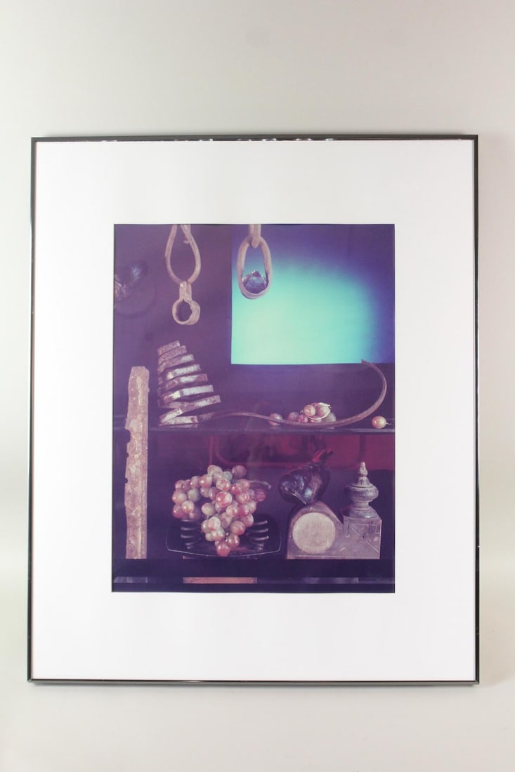 Framed Still Life Color Photograph: Framed Still Life Color Photograph. In a modern twist on traditional still life compositions, this color photograph features grapes, forged iron items and a carved crow, with a luminous aqua glow in t