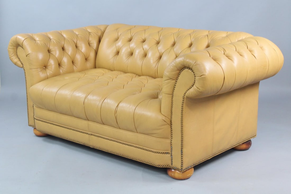 Buttercream Leather Chesterfield Loveseat Sofa: Buttercream Leather Chesterfield Loveseat Sofa. This short couch has button tufted leather upholstery all over and brass studded accents across the front, on rounded wooden bun feet. Dimensions are 29
