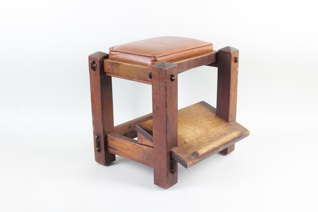 Arts & Crafts Mission Leather Topped Foot Stool: Arts & Crafts Mission Leather Topped Foot Stool. This foot rest has visible joinery connecting the minimalist frame, with an angled surface on the bottom brace and a whiskey colored leather upholstere