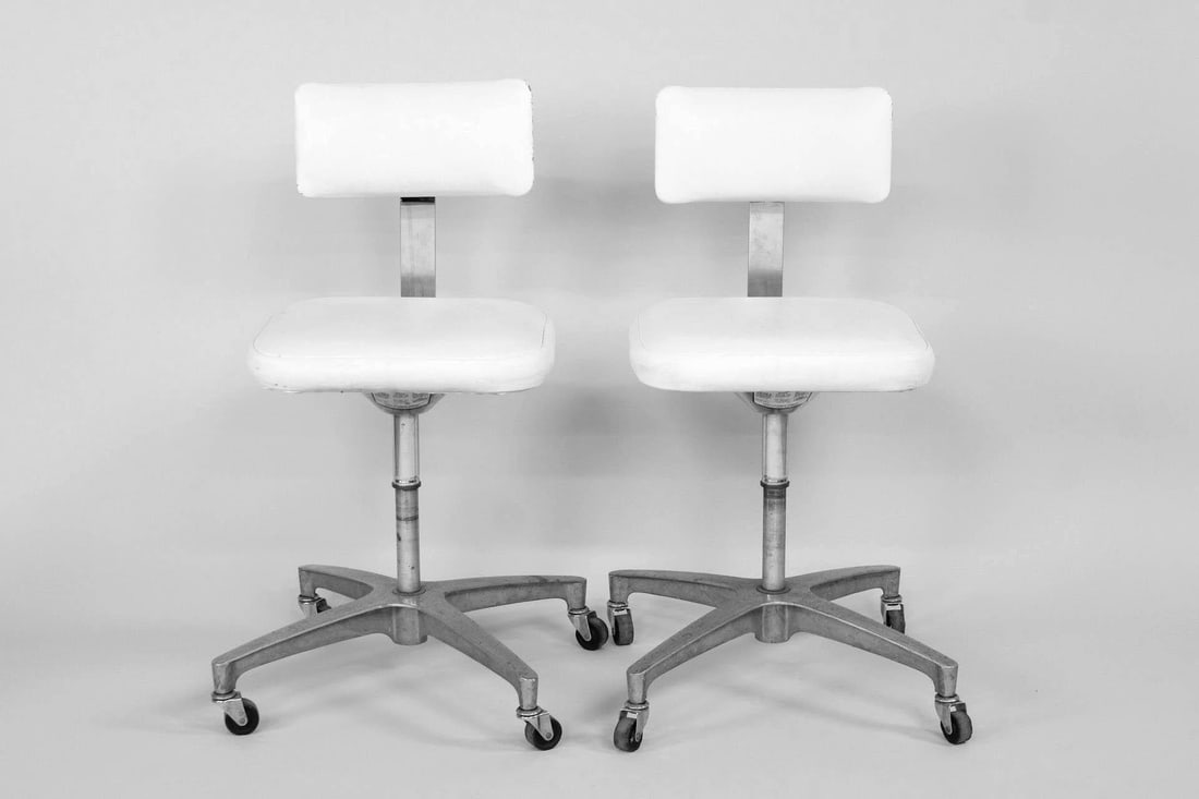 Pair of Industrial Adjustable White Vinyl & Metal Rolling Chairs, Ajusto: Pair of Industrial Adjustable White Vinyl & Metal Rolling Chairs, Ajusto. These medical style rolling stools have metal bases with wheels and a white upholstered back and seat with adjustable height.