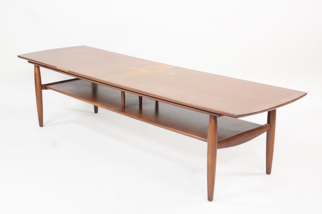 Mid-century Modern Wood Surfboard Coffee Table: Mid-century Modern Wood Surfboard Coffee Table. Classic, elongated coffee table with sculptural legs and one lower shelf. It is made of a warm hued wood, possibly walnut. Dimensions are 16 in h x 19 i