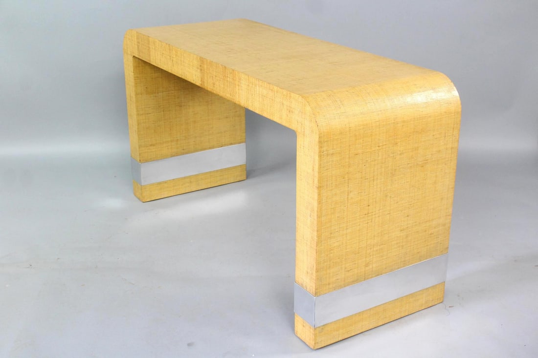 Grasscloth Waterfall Console Table, Karl Springer Style: Postmodern Waterfall Console. A table with continuous, curved lines and silver toned metal accents at the bottom of each leg. The textured grasscloth surface appears to be laquered. Unmarked, in the s