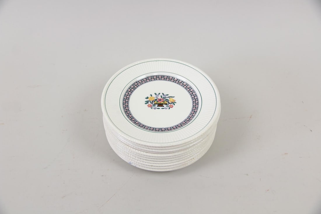 Collection of 11 Wedgwood Trentham Porcelain Floral Plates: Collection of 11 Wedgwood Trentham Plates. These sweet white porcelain plates feature a central flower basket motif and a distinct border design. Marked on the back, Tretham, Wedgwood, England. Dimens