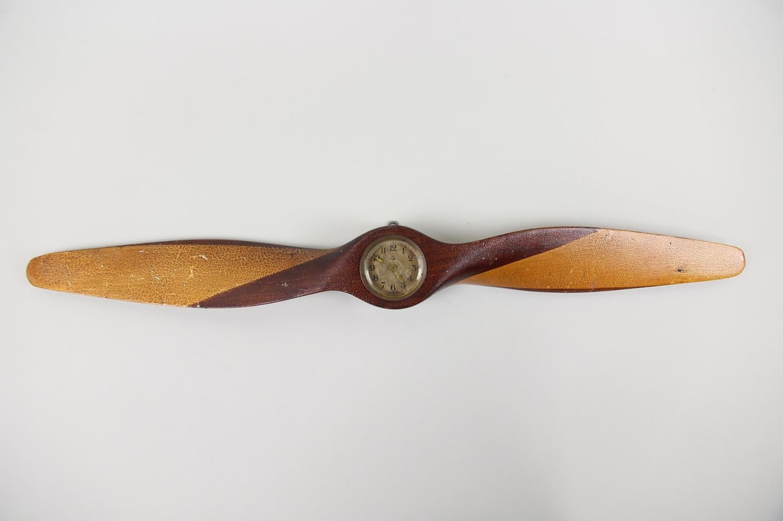Wooden Airplane Propeller Clock: Wall Mount Wood Propeller Clock. Whimsical wall clock made of a small wooden propeller with a clock mounted in the center. Dimensions are 3.25 in h x 28 in w x 1.75 in d. Condition is good with wear a