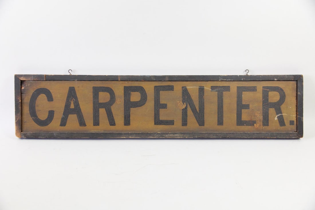 Painted Wood "Carpenter" Sign: Double Sided Painted Wood "Carpenter" Sign. Rectangular wooden sign is painted brown, with black lettering and frame. Dimensions are 10.5 in h x 43.5 in w x 1.5 in d. Condition is good with crazing an