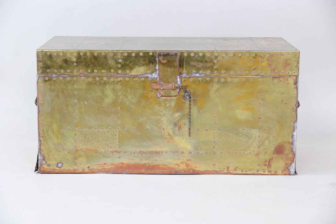 Sarreid Hollywood Regency style Brass Trunk Chest: Brass Clad Trunk With Leather Handles. A sturdy storage trunk with brass-clad exterior and metal studs. It has two leather handles and a chain latch closure. Unmarked, but we believe this is by Sarrei