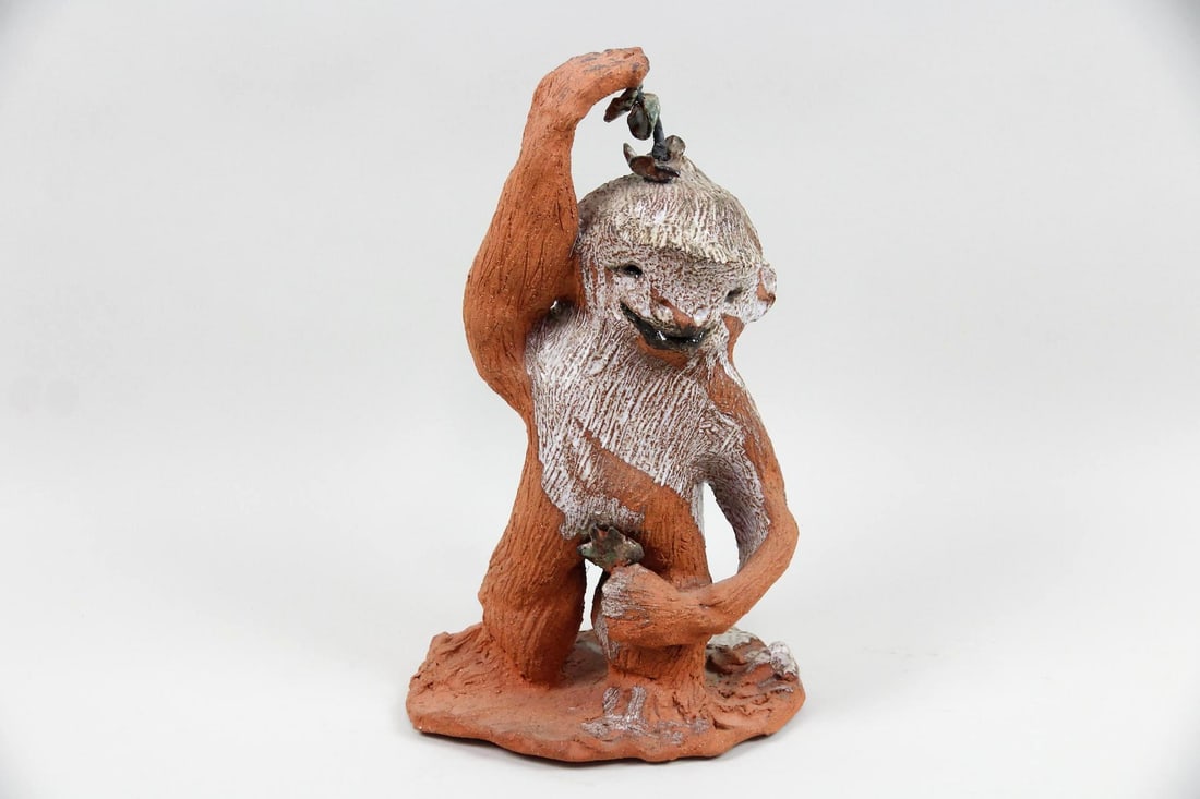 Folk Art Ceramic Monkey Sculpture: Folk Art Ceramic Monkey Sculpture. A hand built ceramic sculpture of a smiling monkey holding a branch in each hand. It has a heavily textured surface and areas of white glaze. Dimensions are 16 in