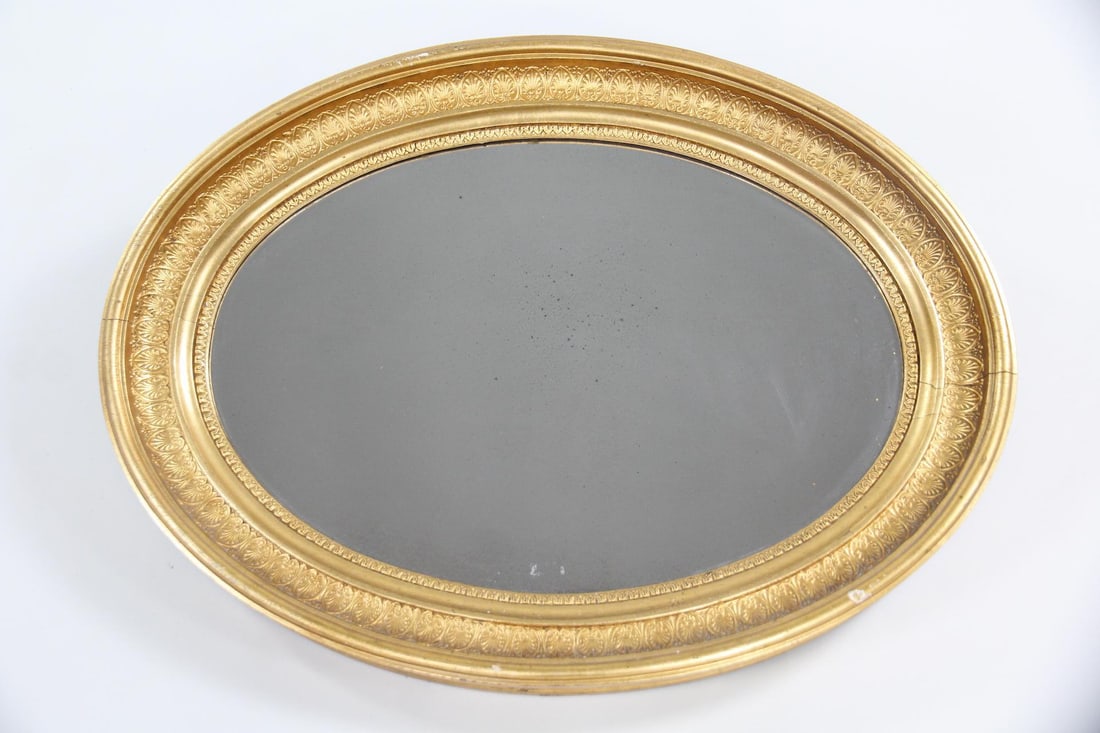 Deep Empire Gold Gilt Oval Mirror, Giltwood Frame: Empire Oval Mirror with Giltwood Frame. Oval mirror with giltwood frame decorated with acanthus leaves and other patterns. Dimensions are 23 in h x 31 in w x 3 in d. Condition is good with a couple of